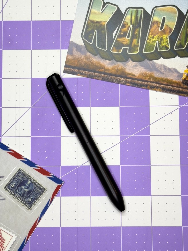 Karas Modal All Black with some free swag from Karas Pen Co on a 1 inch grid background